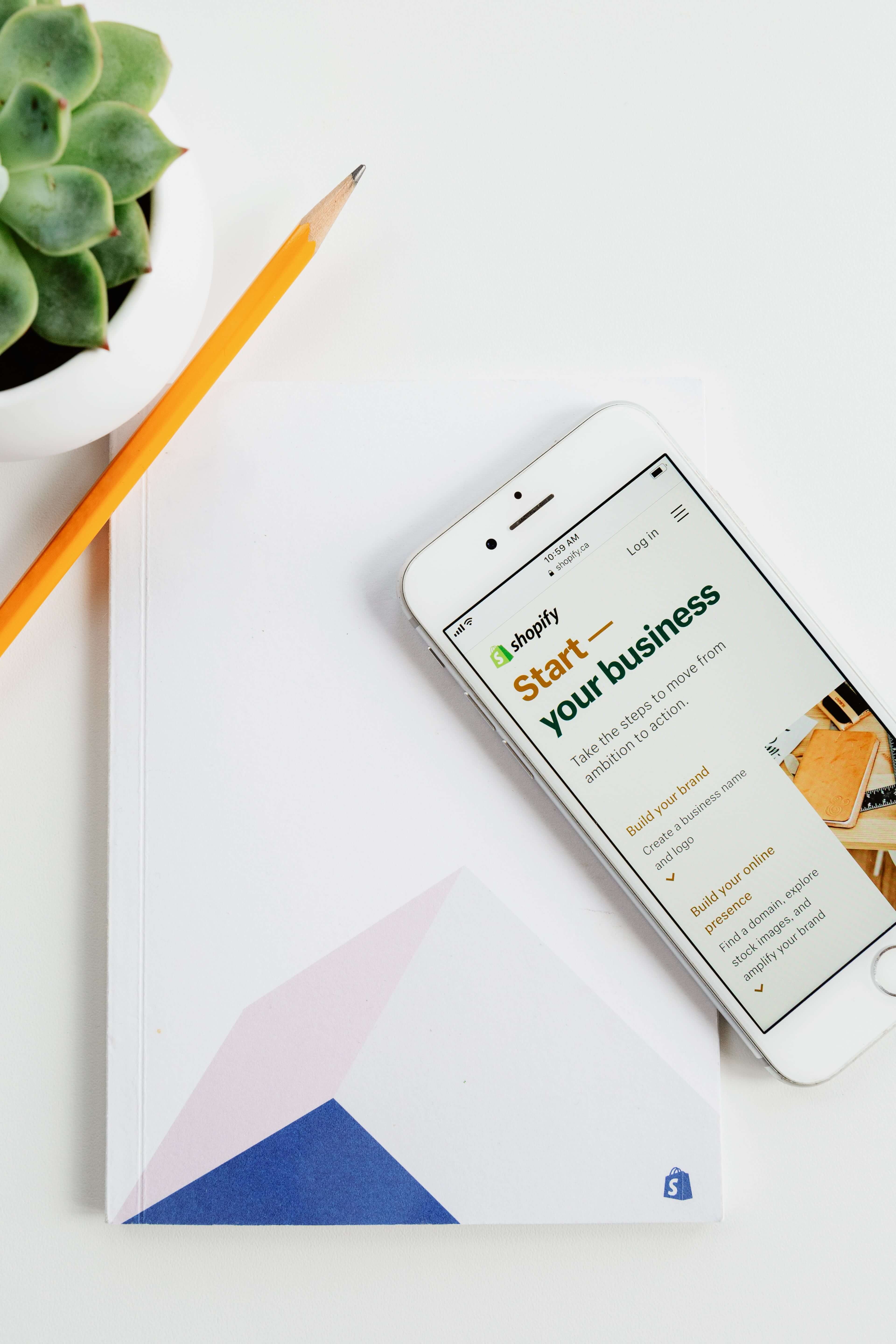 Person using Shopify on a phone with a notepad and pen for Ecommerce web development services